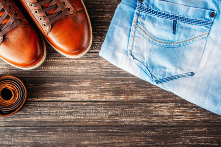 棕色皮革男式靴子, 腰带和蓝色牛仔裤, 深色木质背景, 带复印空间的顶部视图