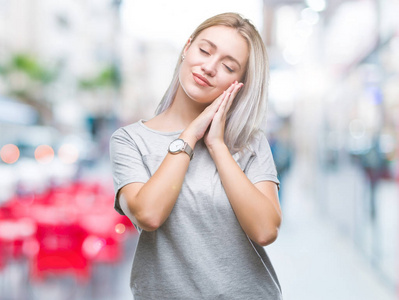 年轻的金发女人在孤立的背景下睡觉疲倦的梦想和手一起摆姿势, 而微笑着闭着眼睛