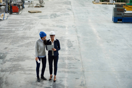 两名现代女工程师的全长画像 hardhats 规划工作在剪贴板上书写的现代工厂车间