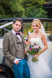 年轻快乐美丽优雅的新婚夫妇站在户外, 依靠汽车