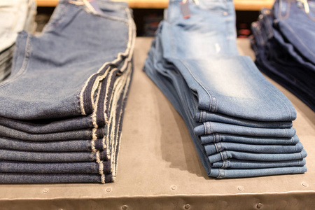一堆蓝色牛仔裤在商店里。购物销售背景主题。商店衣架上的衣服