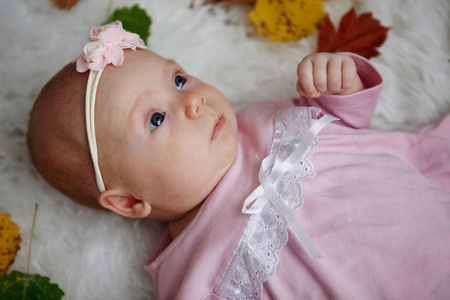 小可爱的女孩两个月大的粉红色的礼服和花在她的头上躺在一个床罩周围的红色和黄色的秋叶