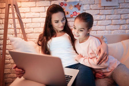 母亲和小女儿看电影在笔记本电脑下灯罩在晚上在家