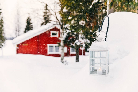 圣诞蜡烛灯笼。红色的木制小屋在农村下雪芬兰。冬季景观