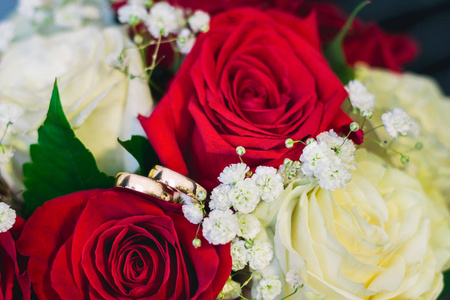 两个金色的结婚戒指躺在新娘花束组成的白色和红色的玫瑰