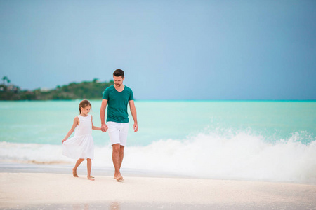 快乐的父亲和他可爱的小女儿在热带海滩一起散步