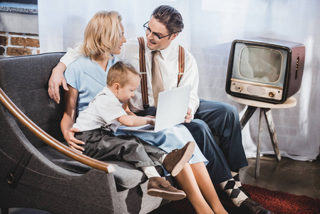 快乐的50s 风格的家庭与一个孩子一起使用笔记本电脑在家里