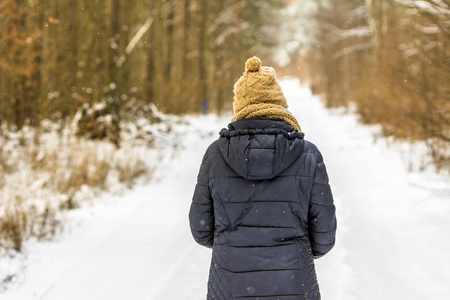 妇女在冬天衣裳在雪在路在森林里漫步