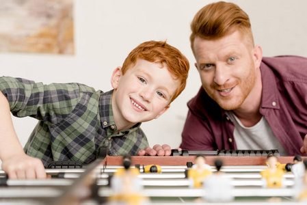 快乐的红头发的父亲和儿子在一起玩桌球时微笑着在家里