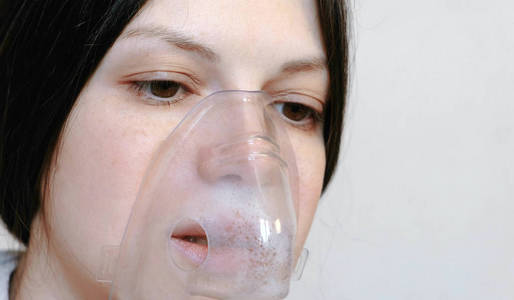 使用喷雾器和吸入器进行治疗。特写年轻女人的脸吸入吸入口罩。前视图