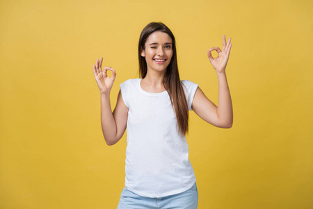 幸福的年轻女人，显示 ok 的手势，用手指眨眼隔离在黄色背景上