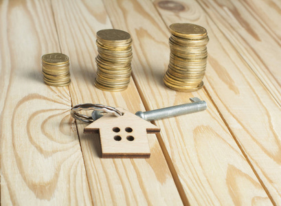 房地产或租赁物业的概念。木制背景下的钥匙和硬币的房子符号