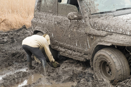 男人放在一辆越野汽车的车轮下, 在泥浆中的泥站里沾上液体泥浆。