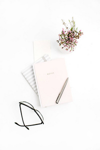 女性博客作文中有笔记本眼镜钢笔和野花的白色背景。平躺, 顶部视图