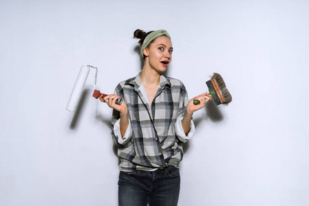 一个滑稽的年轻女孩穿着旧衣服在她的公寓里修理, 拿着一只刷子和一把滚筒来粉刷墙壁, 不能选择