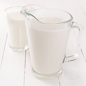 白色木制背景的水壶和牛奶杯