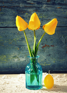 黄色郁金香在玻璃花瓶, 蜡烛在蓝色木质背景