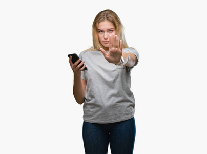 年轻的白种人妇女发送消息使用智能手机在孤立的背景与开放的手做停止标志与严肃和自信的表达, 防御手势