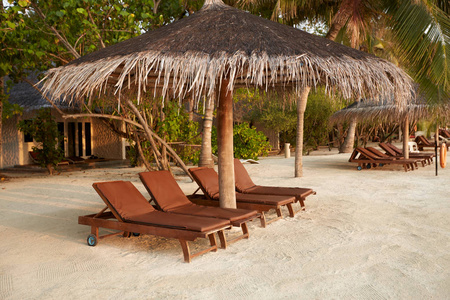 在稻草伞下的沙滩甲板椅。马尔代夫岛上的印度洋海岸线。白色沙滩和平静的大海。旅行和度假概念