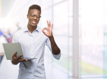 年轻的非洲裔美国商人使用电脑笔记本电脑做 ok 标志与手指, 优秀的符号