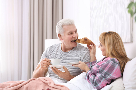 成熟的夫妇在床上吃早饭。浪漫的早晨