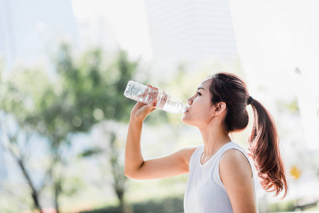 一个年轻的亚洲妇女在公园慢跑后从水壶里喝水的镜头