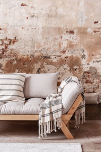 木灰色沙发上的图案毯子和枕头, 在平坦的室内装饰有红色砖墙。真实照片