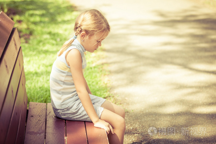 悲伤的小女孩坐在公园的长凳上,在白天的时间