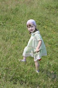 漂亮的小女孩穿着用鲜花走在草甸在汇总