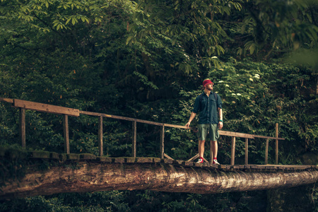 旅行者穿过悬挂在绿色夏日森林中的桥