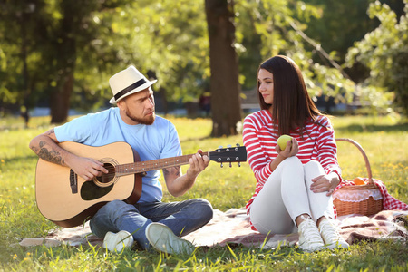 愉快的夫妇与吉他休息在野餐在春天公园