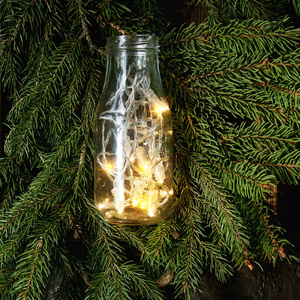 圣诞彩灯在玻璃瓶上的花环上, 绿冷杉树枝上的暗纹理背景。圣诞节日心情卡片。带空间的顶部视图。方形图像