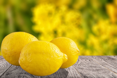 黄色花朵背景下的木表面上的柠檬