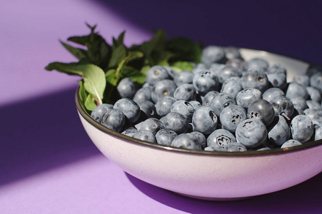 新鲜美味的蓝莓与薄荷在碗紫色背景