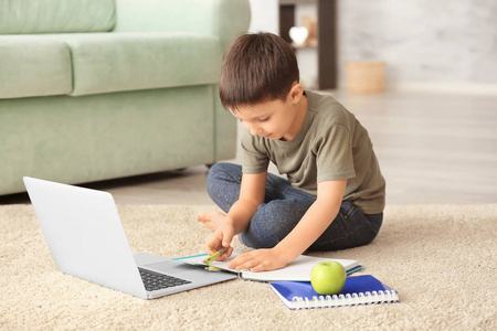 在室内做家庭作业时使用笔记本电脑的可爱小男孩