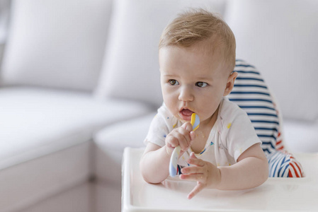宝贝用勺子。食物, 孩子, 喂养和人的概念婴儿与勺子坐在高脚和在家吃。高椅上的快乐男孩肖像