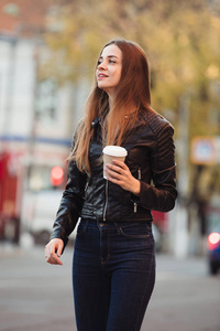 美丽的妇女持有纸咖啡杯和享受在城市散步
