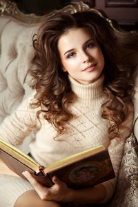 坐在舒适的椅子与书在手的年轻妇女