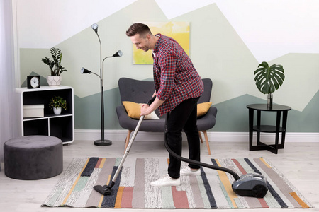 年轻人在家里用吸尘器清除地毯上的污垢