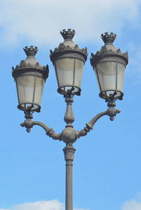 在蓝天的映衬下, 可以看到一个灰色的巴黎灯柱。它有三个玻璃灯, 华丽的灰色外壳。它们是未被点燃的