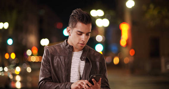 千年拉丁裔男子晚上在城市街道上接听手机