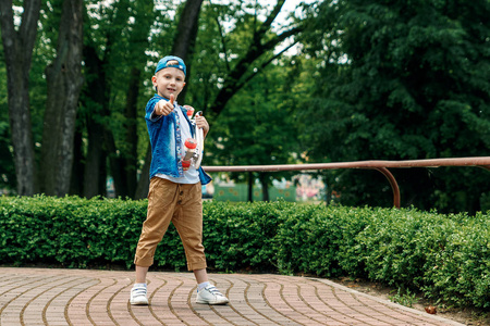 一个小城市男孩和一个滑板。一个年轻人站在公园里拿着滑板。城市风格。城市的孩子。孩子学会骑滑板