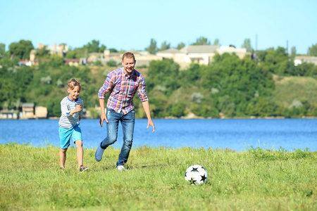 快乐的父亲和儿子在河边踢足球