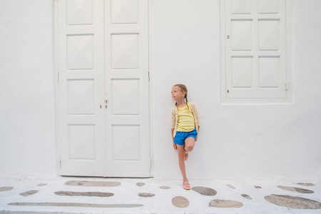 在户外在古老的希腊村庄的小女孩画像。孩子在希腊村庄与白色的墙壁和多彩门街