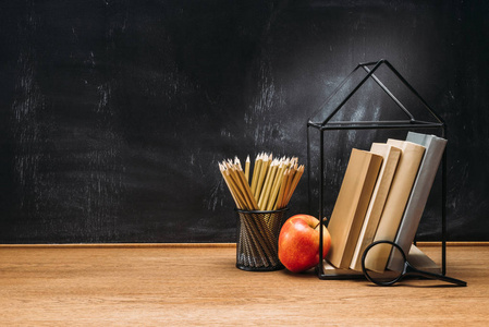 关闭新鲜苹果, 放大镜, 铅笔和书本上的空白黑板后面的木表面的看法