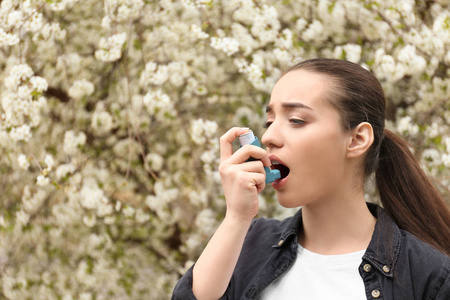 年轻妇女使用吸入器附近开花树。过敏概念