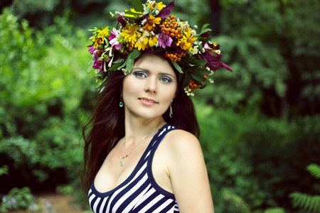 一个美丽的女人的肖像微笑着她的头在夏季公园的花朵花圈