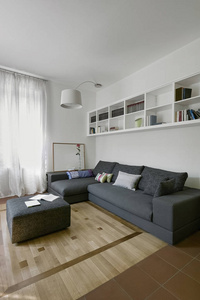 室内拍摄的现代客厅的地板是由木材在前景灰色织物脚凳和底部灰色织物沙发