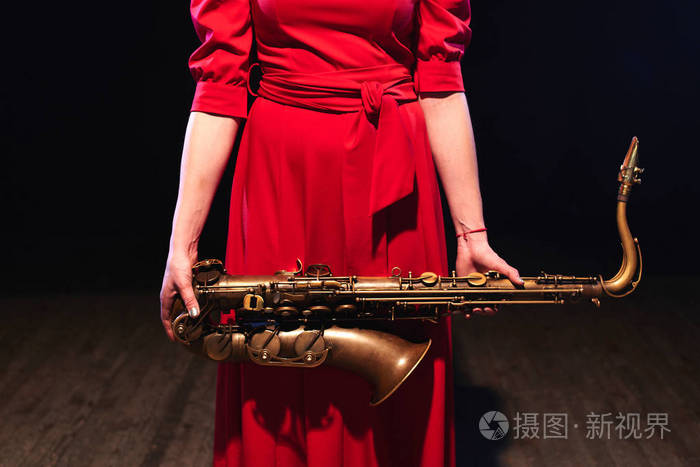 音乐家妇女在明亮的红色礼服拿着萨克斯在手特写