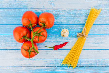新鲜有机西红柿与 Waterdrops 大蒜红辣椒和未煮熟的意大利面食与表带在蓝色和白色的背景与空空间高对比度顶部视图